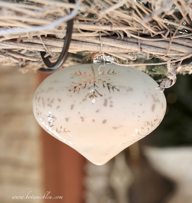 Hang a mercury glass Christmas ornament in the center of a horizontal wreath above a dining table.