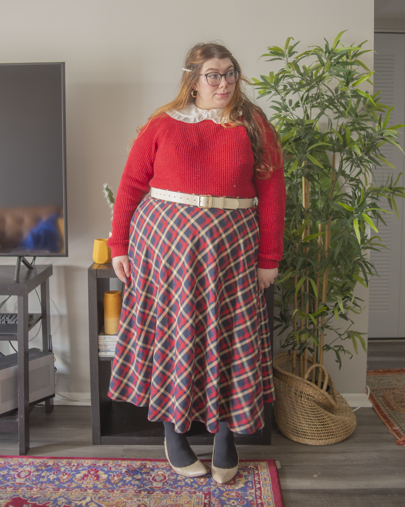 An outfit consisting of a redcrew neck sweater tucked into a red and blue plaid midi skirt and cream slingback heels.