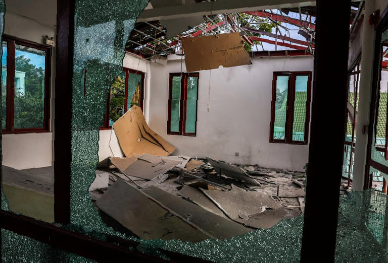 Shattered windows mirror Thailand’s closed border, reflecting broken promises of universal care.