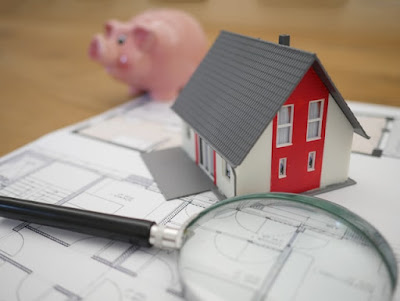 A magnifying glass, a small house, and a piggy bank behind them