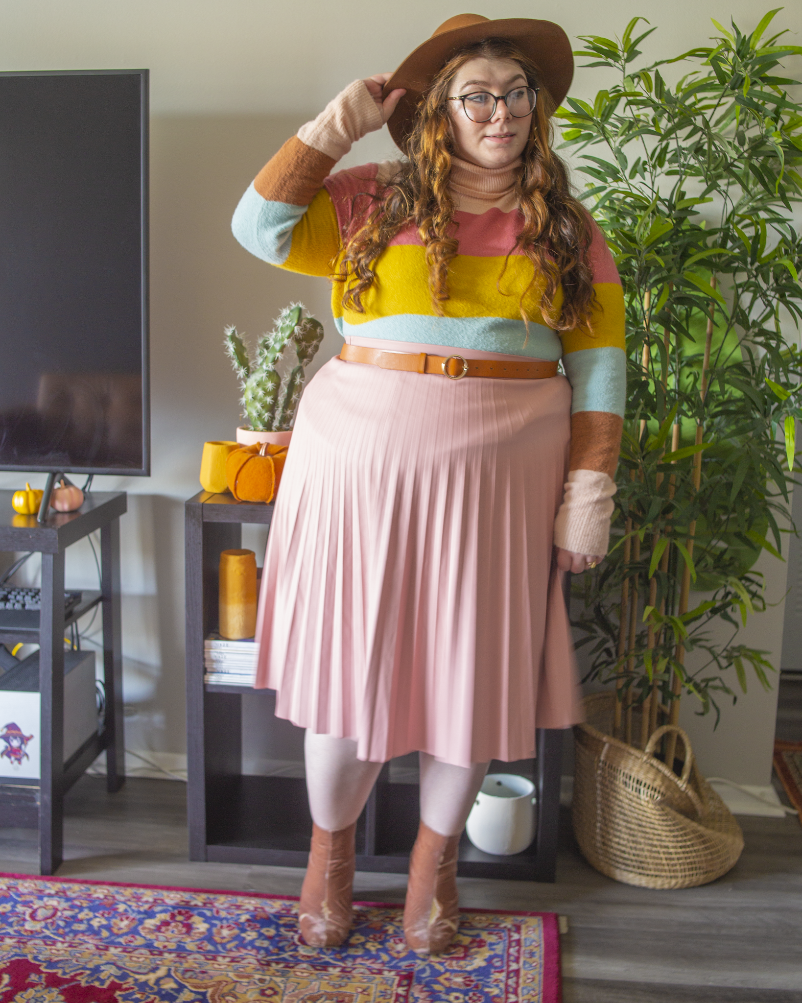 An outfit consisting of a pastel pink beret, a light brown, pastel pink, pastel blue and marigold yellow turtleneck tucked into a pastel pink faux leather midi skirt and pink velvet midi boots.