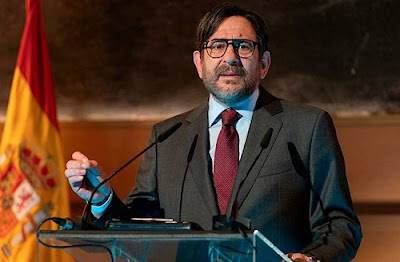 Un hombre da un discurso en un atril con la bandera española de fondo