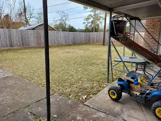 A backyard with a fence and a ride on car on cement.