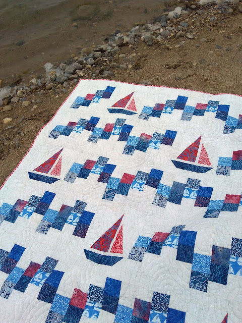 Patchwork quilt.  Blue and red on a light background.  Sailboat blocks and squares arranged in a wave pattern.
