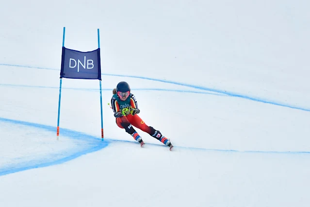 Canadense contorna bandeira azul de circuito de esqui alpino. Ele veste uma malha vermelha com detalhes em branco e amarelo e um capacete azul