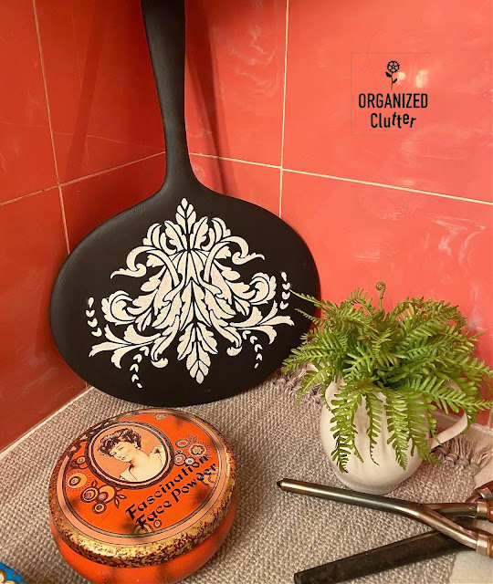 Photo of a black painted hand mirror stenciled with a scrolly stencil in a vintage bathroom vignette.