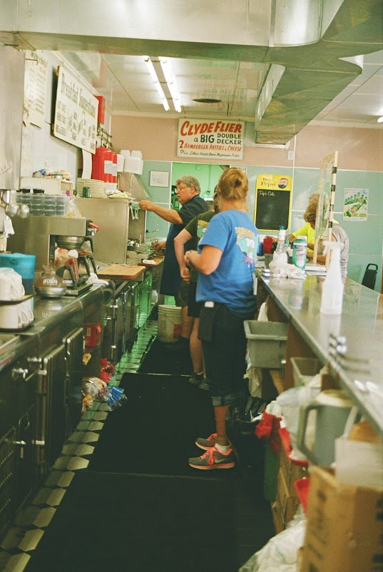 Workers in the food prep aisle behind the customer counter at a diner.