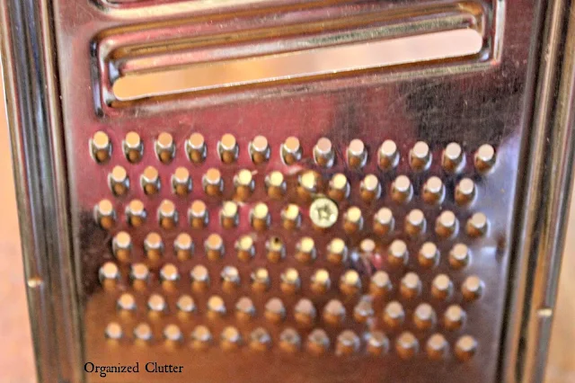 Photo of a kitchen grater being screwed to a piece of wood.