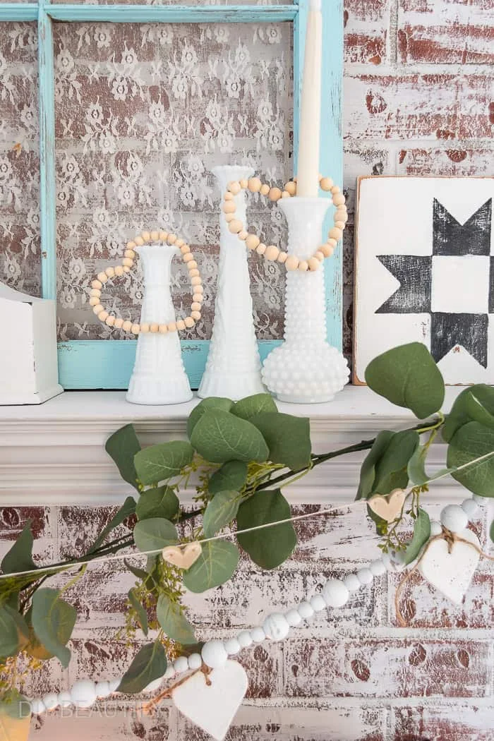 beaded wood hearts hanging on milk glass vases, green garland