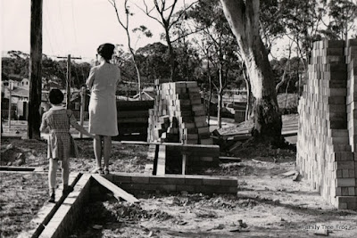 B&W photo of school child and mother standing on the foundations of new home