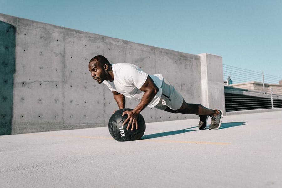 A black man in a white t-shirts and gray shorts doing push ups using training ball to lose weight