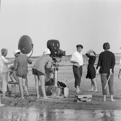 black and white photograph of directo Fellini giving instructions on beach set of "La Dolce Vita"