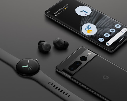 A black Pixel 7 Pro showing the triple camera system. There are also Pixel Buds, and the Pixel Watch showing the screen. The screen of one of the Pixels is showing the icons and the black wallpaper.