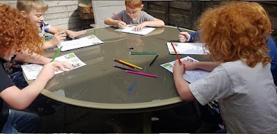 Group of 5 boys colouring together at a table outdoors