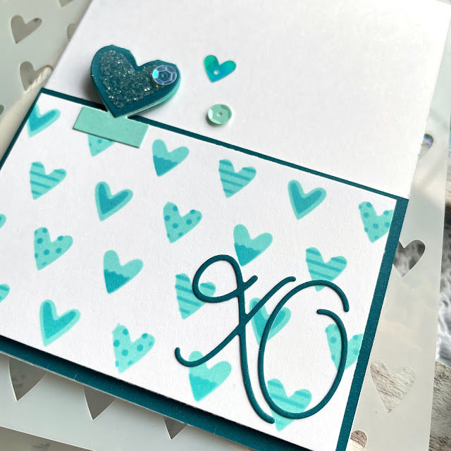Teal XO Valentine's Day card made with: Scrapbook.com heart patterns stencil; tabs 1 and 2 dies, loopy cursive dies, jewels and peppermint smooth cardstock, mint tape, domed foam blending tool; Tim Holtz salvaged patina and peacock feathers distress oxide ink, rock candy glitter; 28 Lilac Lane heart of atlantis sequins