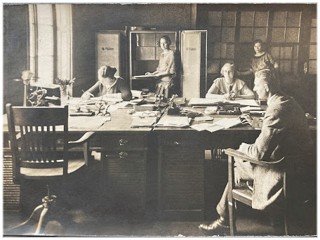 Historische Fotografie, die Büroleben zeigt: Schreibtische, Telefon, Bleistifte, Mitarbeitende