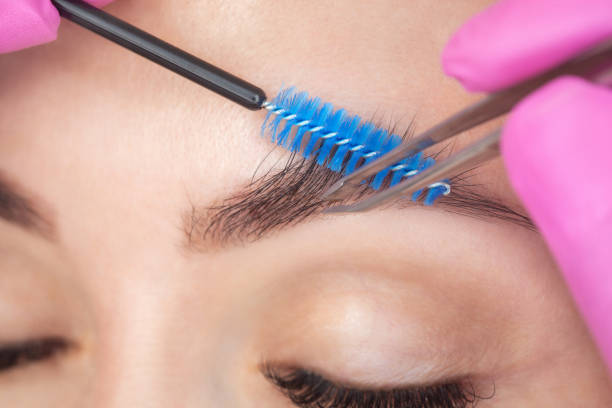 A woman combing her eyebrows with a spoolie ad plucking it a tweezer