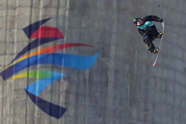 Su, de azul e capacete preto, salta com o logo de Pequim 2022 ao fundo