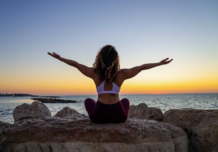 A fitness woman in white sleevles top and a tight-fitting pants sitting on a rock meditating to lose weight