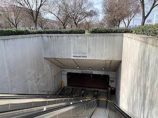 Photo of three elevators descending into a concrete arched entrance. There are small letters reading "This station is dedicated to CARMEN E. TURNER" and "Smithsonian Station"