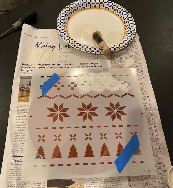 Photo of a round wooden tray being stenciled with a Christmas Sweater stencil.