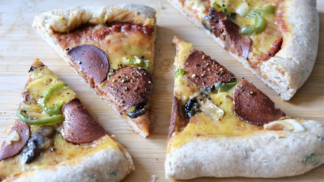 Vegan pepperoni, green pepper, mushroom and onion pizza slices with black cracked pepper on a light wooden chopping board