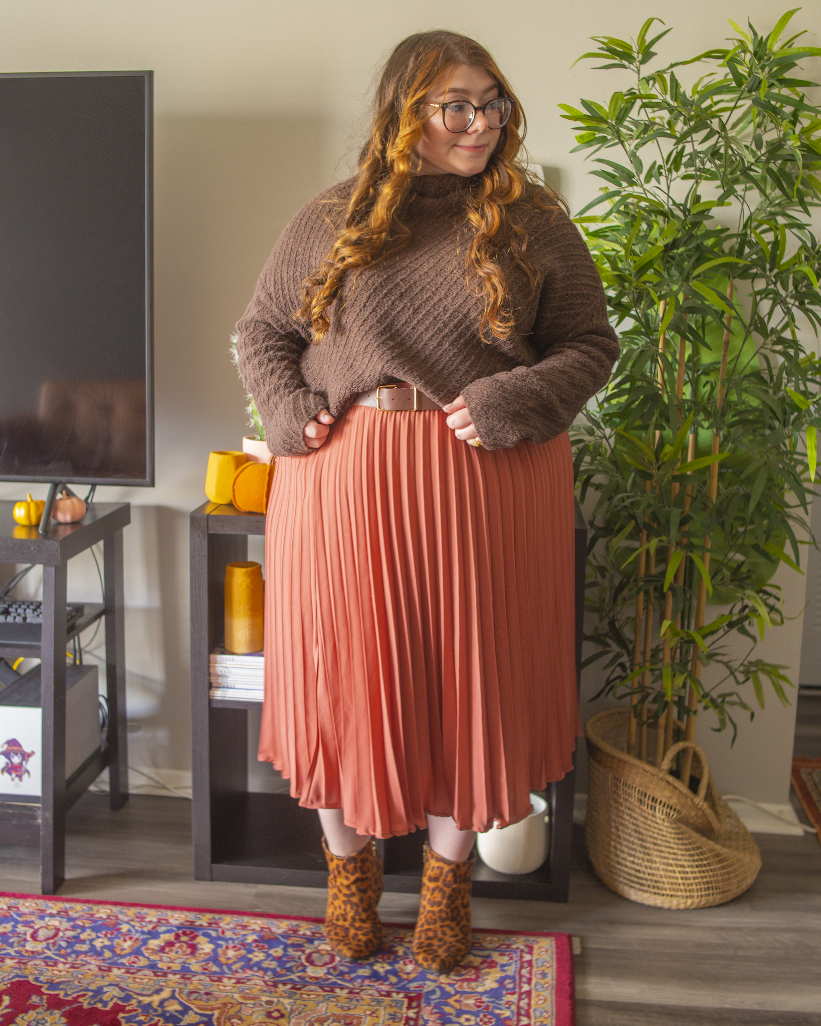 An outfit consisting of a dark brown mockneck sweater half tucked into a rose colored pleated midi skirt and black on brown cheetah print ankle boots.