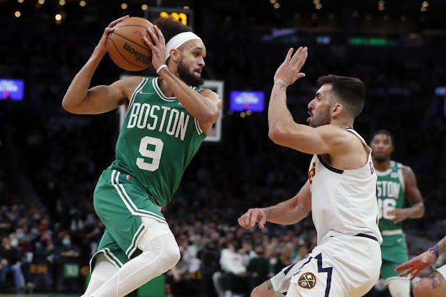 Derrick White in the middle of an athletic play and about to pass the ball while being guarded by a Denver Nuggets player