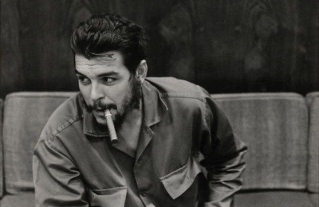 A fotografia mostra Che Guevara, provavelmente posando para a câmera,  sentado em um sofá. Em sua boca há um charuto e ele, vestido com uma camisa de mangas longas, não olha diretamente para a câmera.