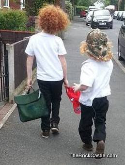 School children walking down the road away from us wearing uniform and sun caps