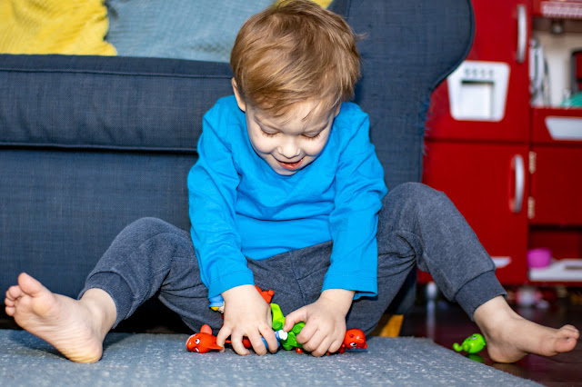 A toddler gathering up a handful of plastic Morphle related mini figures towards him