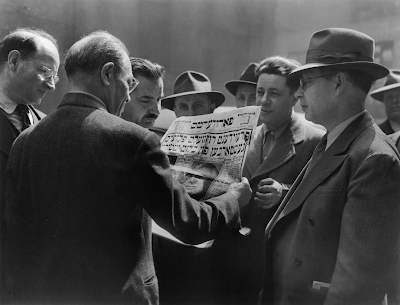 black and white photo of men in the Garment District reading a newspaper in Yiddish about President Roosevelt’s Death, NYC, 1945,” Ida Wyman.
