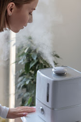 A woman leaning over a white humidifier spewing mist.