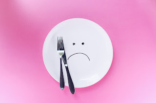 An empty plate with a frown drawn on it in black marker pen. A fork and knife lie next to the plate.