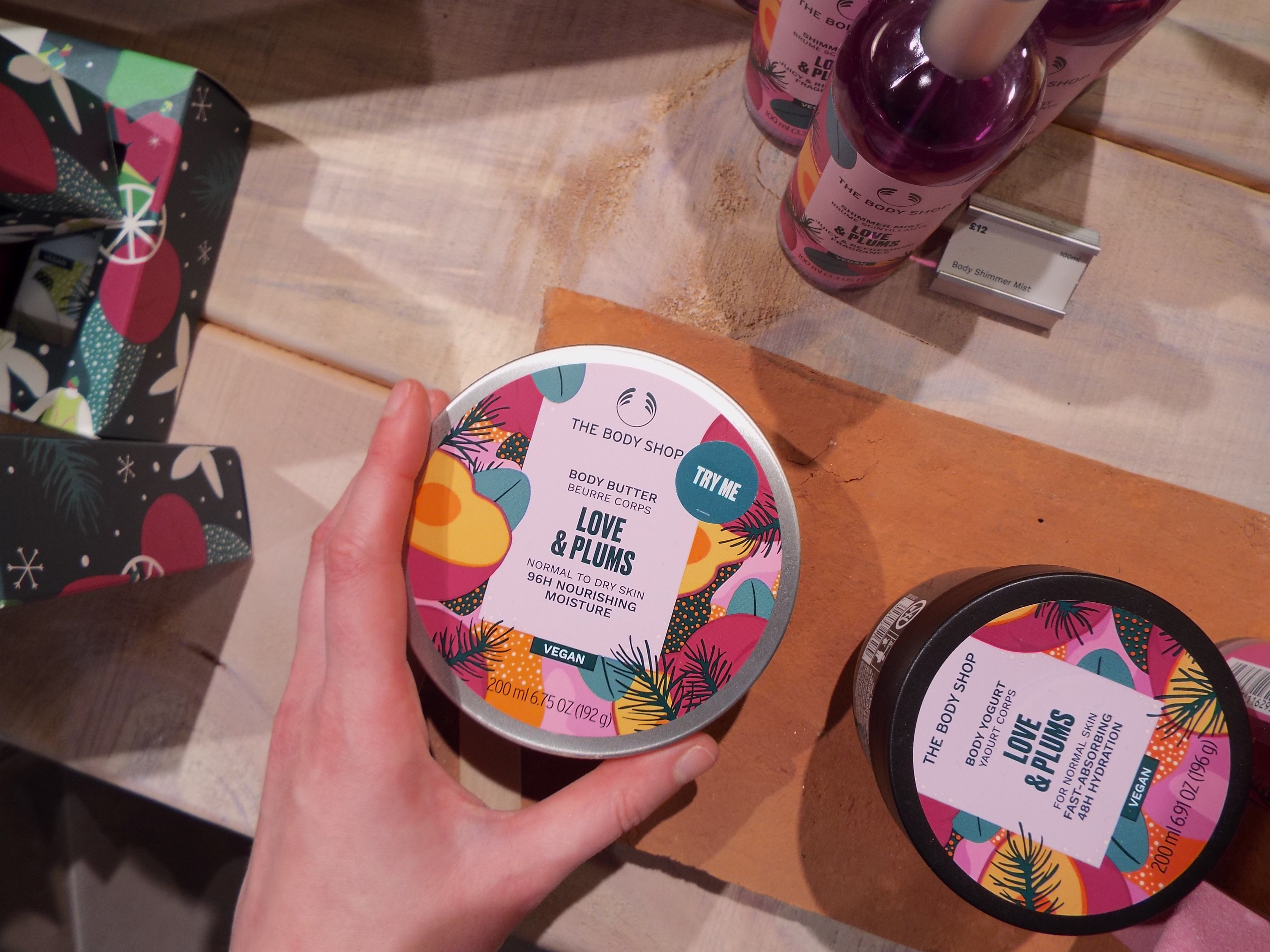 Me holding a tub of the Love and Plums Body Butter amongst the display on the wooden display unit.