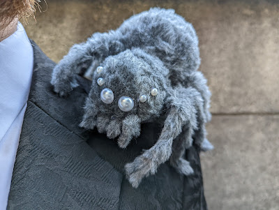 photo of handmade fuzzy gray spider with pearl bead eyes sitting on man's shoulder