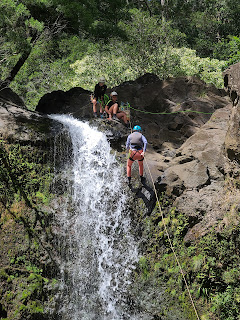 Adult female in pink leggings and a blue shirt rappelling down a waterfall