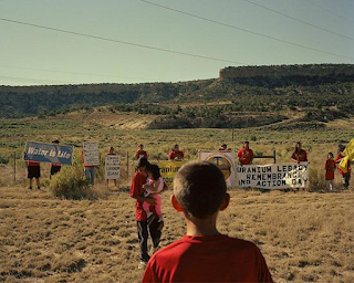 color photograph of residents from Navajo communities, some with protest signs,  gathering on Uranium Remembrance Day, Church Rock, NM July 16, 2016