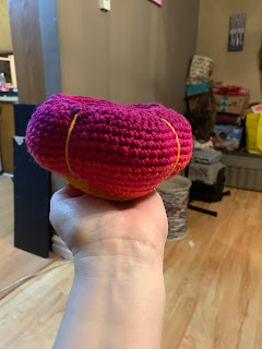 A vaguely gourd shaped crocheted bowl. The color changes, top to bottom, from plum to magenta to orange to orange-yellow. The "bumps" are delineated by straight stitch embroidery in the orange-yellow color.