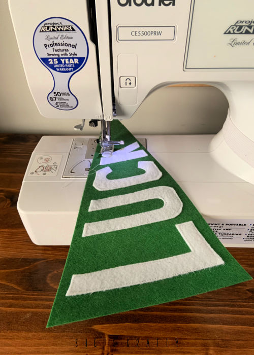 Sew white felt letters onto green flag with sewing machine.