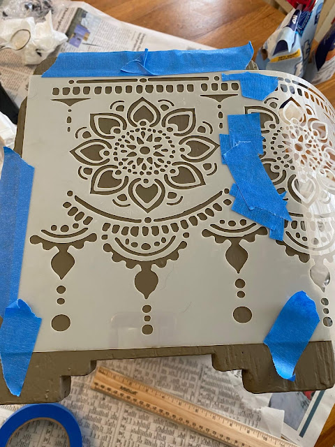 Photo of the Lotus Bloom stencil from Dixie Belle Paint Company being applied to the end of an old footstool.