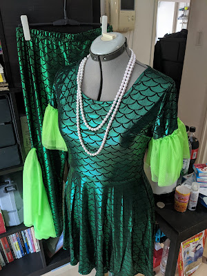 photo of the scale-print dress on a dress form with the leggings hanging on a shelf in the background, with the fin fabric sewn to the dress sleeves