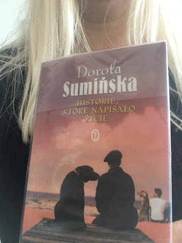 Historie, które napisało życie autorstwa Doroty Sumińskiej prezentuje blondynka o długich włosach, ubrana w czarną bluzkę.