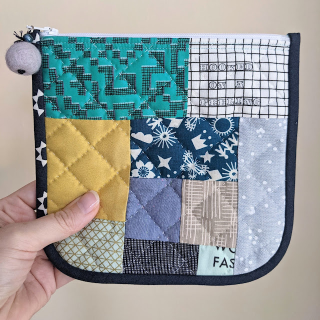 A fabric zippered pouch made with patchwork fabric scraps and hand quilted with a cross hatch pattern