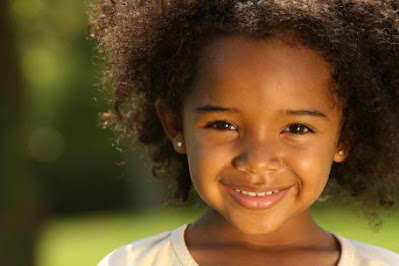 Cute little black girl smiling with a sunny green grass background