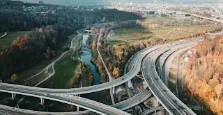 Aerial view of Germany’s Autobahn, a multi-lane highway winding through lush greenery and autumn-colored trees, with cars speeding along the open road.