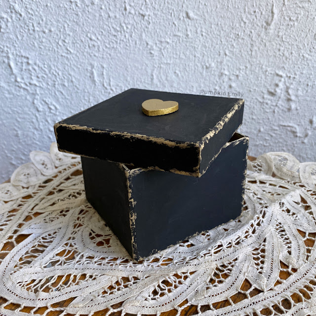 Black vintage/worn down box with a gold heart on the lid.