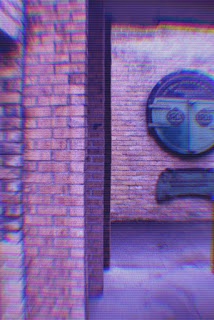 cyberpunk filter of grainy pink of a brick alley with a large, round, copper sign at the end of it