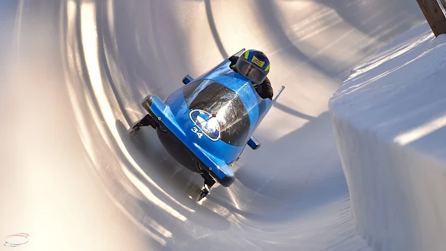 Trenó brasileiro desce a pista de Saint Moritz. O trenó é azul com detalhes em preto. Apenas a cabeça de Edson Bindilatti é visível, com um capacete azul e amarelo