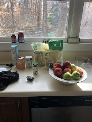 A bowl of apples, some baking ingredients, and a dish towel sitting on the kitchen counter to the left of the kitchen sink.